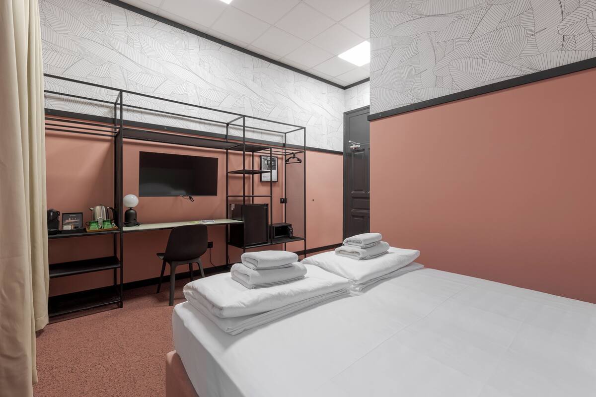 Ein Hotelzimmer mit Etagenbetten, einem Schreibtisch, einem Stuhl, einem Fernseher und einem Bett mit ordentlich gefalteten Handtüchern.
