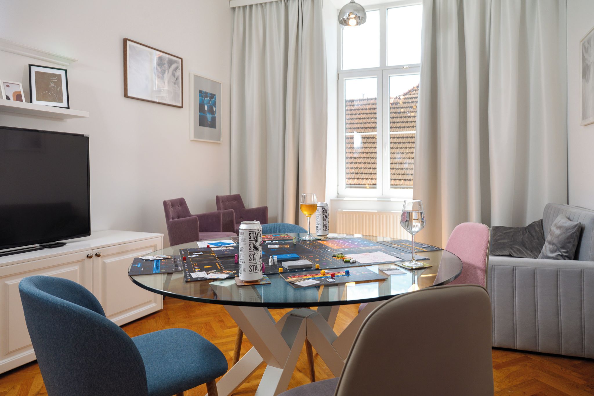 A modern living room with a glass-top table, chairs, a television, and artwork on the walls.