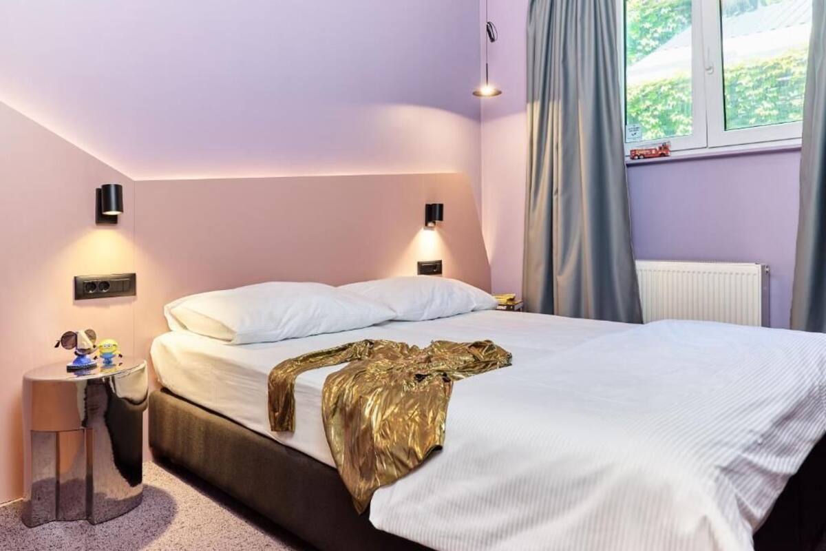 Ein Hotelzimmer mit Bett, Nachttischlampen, einem kleinen Tisch mit Spielzeug und einem Fenster mit Vorhängen.