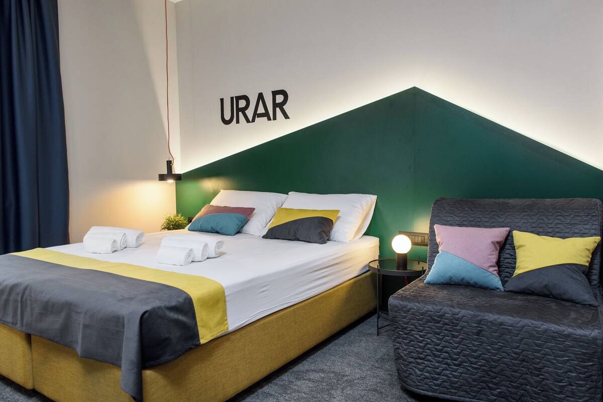 Ein Hotelzimmer mit Bett, einer Couch, einer Wandleuchte und einer Wand, auf der das Wort 'URAR' zu sehen ist.