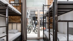 Habitación de un hostal con literas, una bicicleta afuera y una pared de ladrillo.