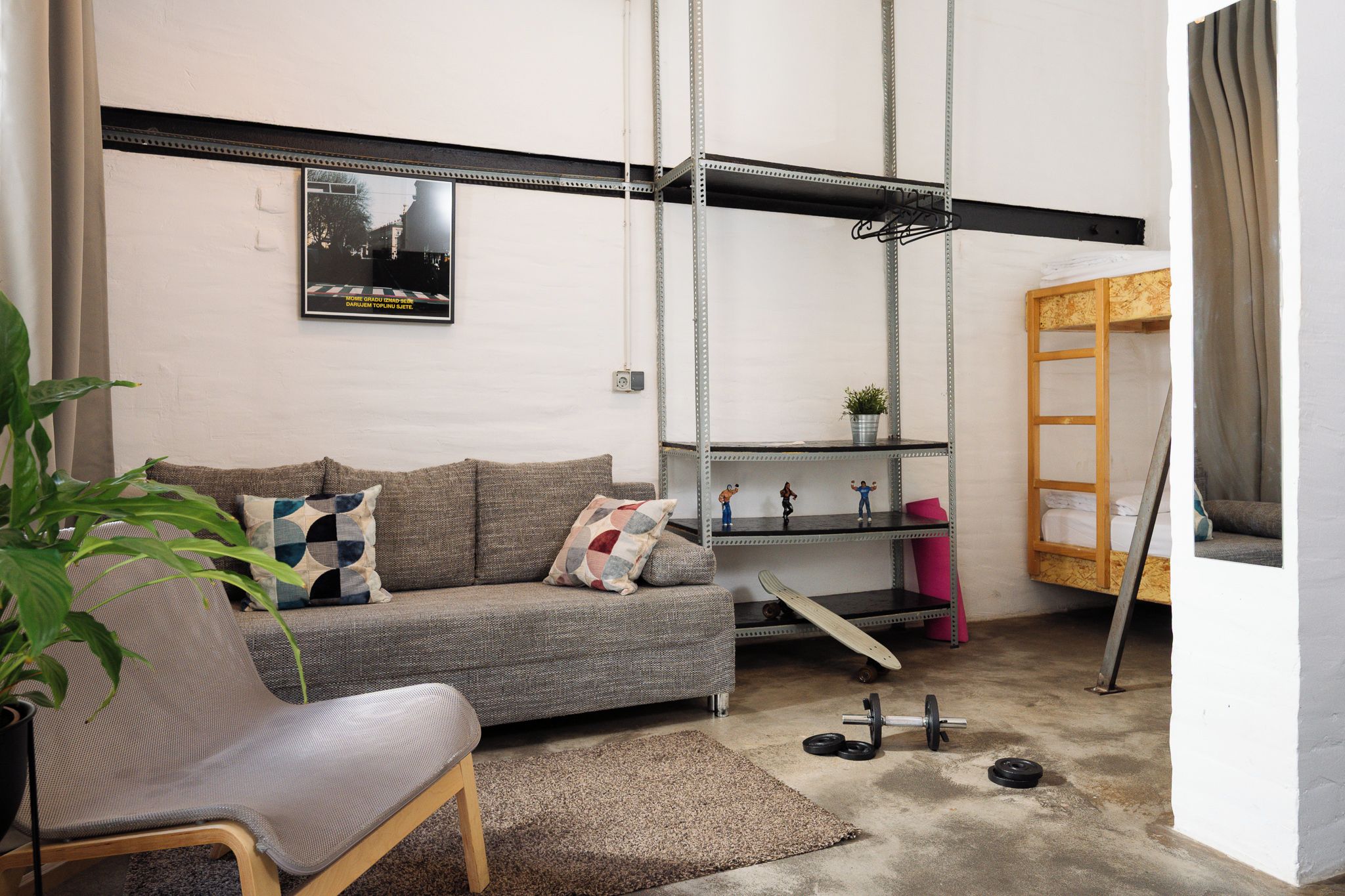 Un espacio habitable compacto con sofá, una silla pequeña, un estante metálico y una cama nido.