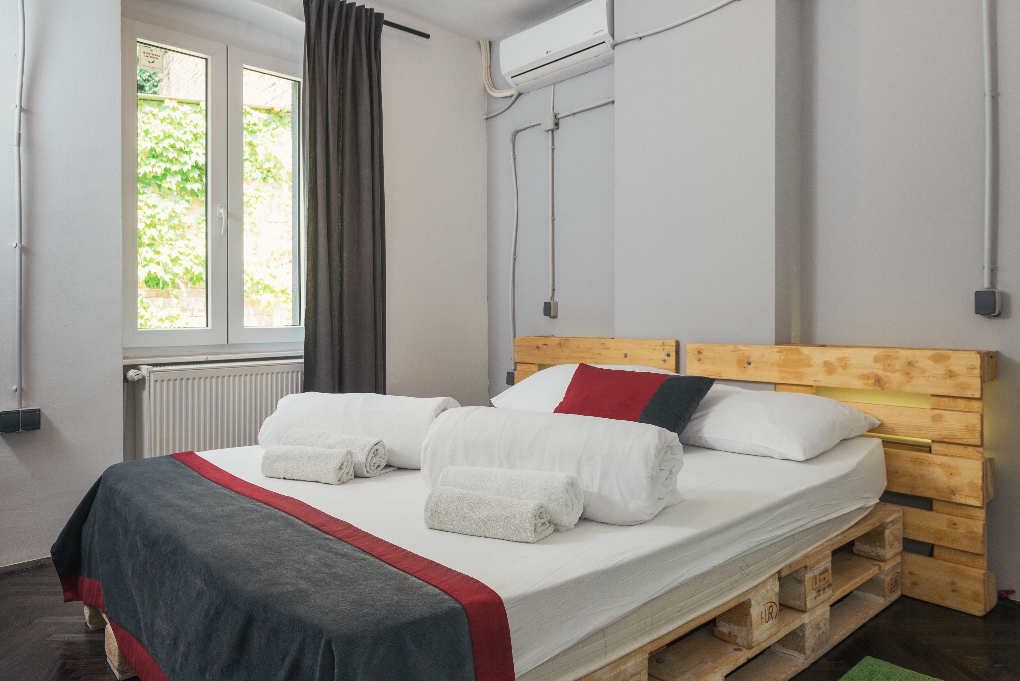 Uma cama de solteiro com cabeceira de madeira, roupa de cama branca e edredom vermelho e cinza.