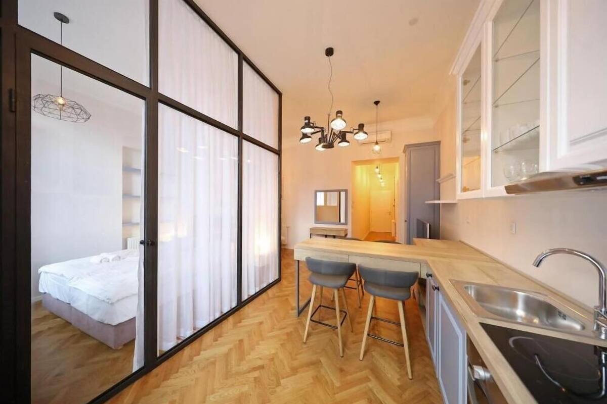 Eine moderne Küche mit Holz-Fischgrätparkett, einer Bar mit Hockern und einem großen Fenster mit durchsichtigen Vorhängen.