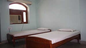 A room with two wooden beds, a window with an air conditioning unit, and a wall-mounted shelf. - Rainbow Guest House (Gaya)