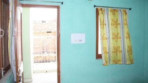 A room with a door leading to an outdoor area, a window with a curtain, and a wall-mounted electrical outlet. - Rainbow Guest House (Gaya)