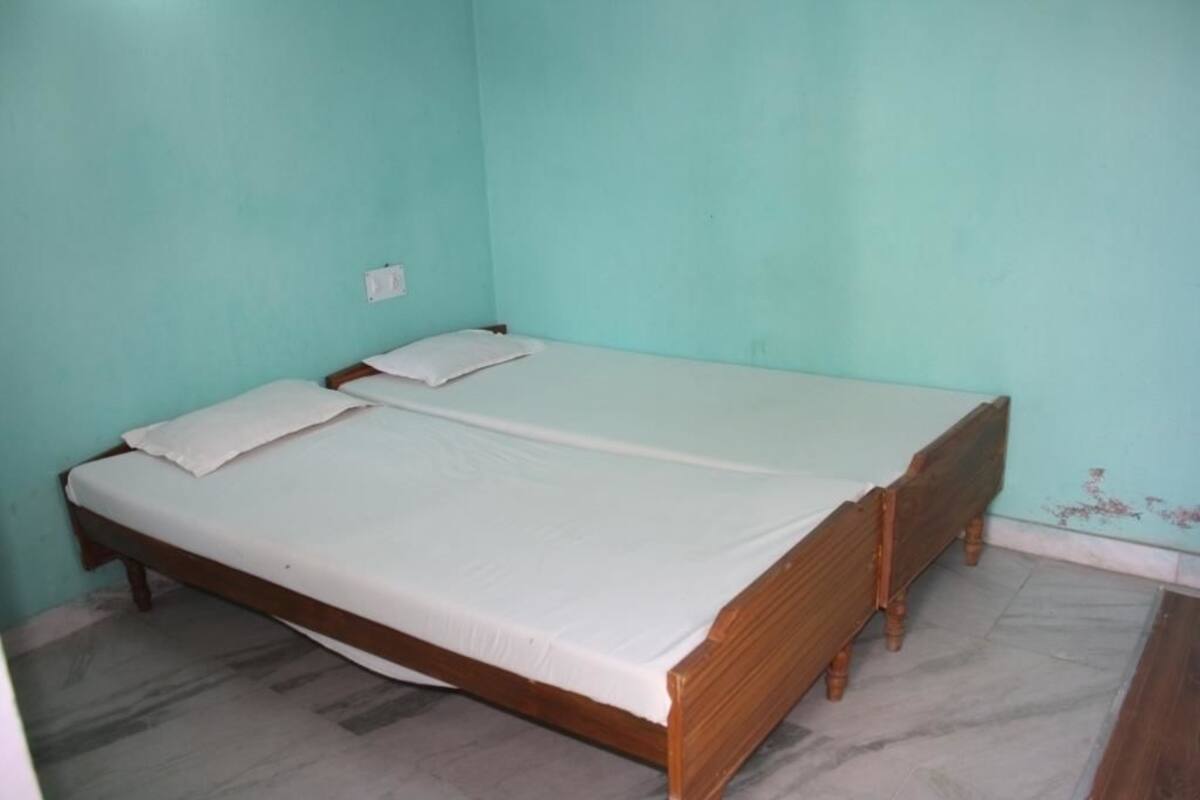 A single-bed room with a wooden frame, white bedding, and a light teal wall.