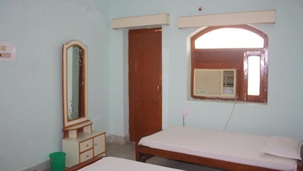 A bedroom with a single bed, a dresser, a mirror, and a door. - Rainbow Guest House (Gaya)