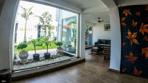 Ein geräumiger Raum mit einem großen Schiebeglastür, die zu einem Garten führt, einem Deckenventilator und einem schwarzen Sofa mit Kissen.
