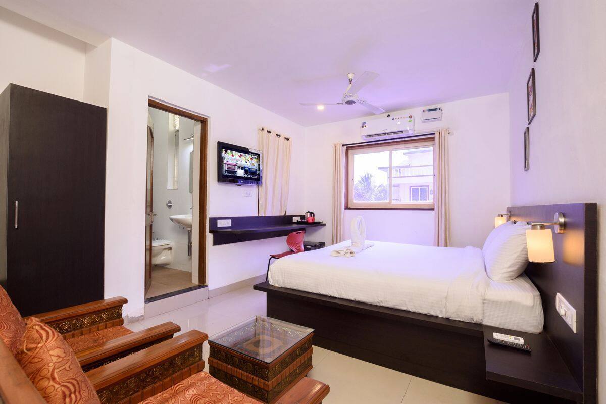 Een hotelkamer met een bed, een televisie, een plafondventilator, een raam met gordijnen, een nachtkastje en een bank.