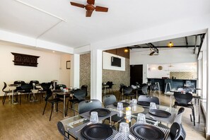 A modern dining area with black chairs and tables, a ceiling fan, and a kitchen in the background.