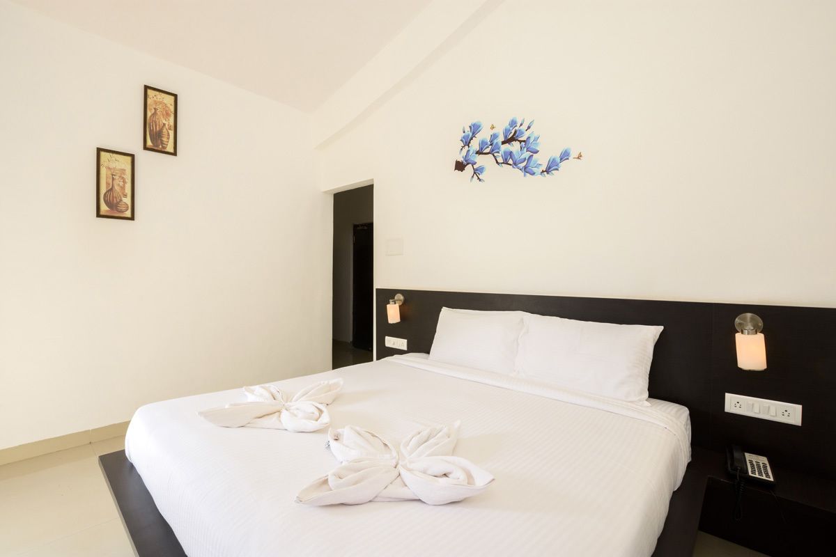 Habitación de hotel con una cama grande, ropa de cama blanca, cabecero negro y un teléfono montado en la pared.