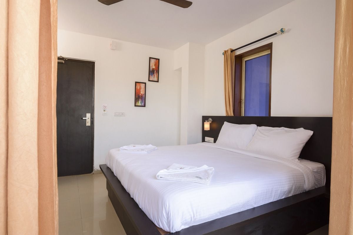 Una habitación de hotel con una cama, una puerta, un ventanal con cortinas y dos luces fijadas a la pared.