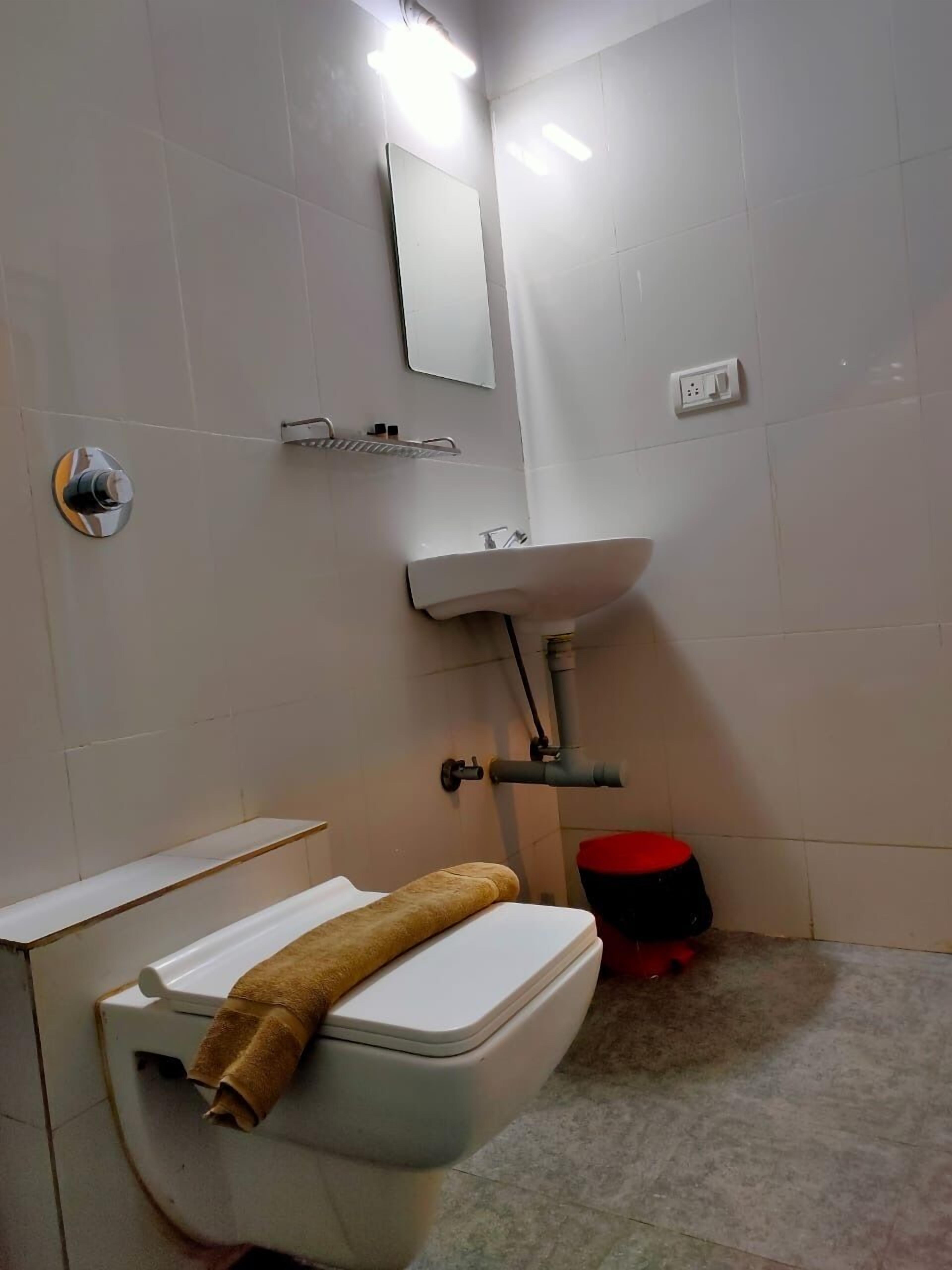 Un baño con inodoro, lavamanos, espejo y un balde rojo.