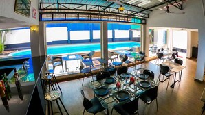 Ein Restaurant mit Blick auf einen Pool, Tische und Stühle für das Essen und eine Decke mit Ventilatoren und Lampen.