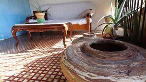 A room with a patterned floor, a wooden coffee table, a sofa, and a large decorative pot. - Hostal La Solana (Arenas de San Pedro)