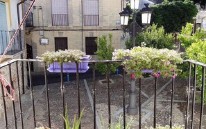 Un balcon agrémenté de plantes en pot, d’où l’on peut admirer un immeuble avec des fenêtres et une porte.
