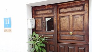 A wooden double door with a brass handle, a white wall, and a blue sign with white lettering. - Hostal La Solana (Arenas de San Pedro)