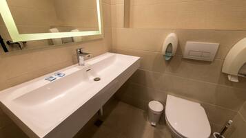 A modern bathroom with a white sink, mirror, toilet, and hand dryer.