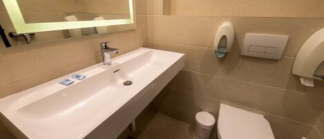 Un baño moderno con lavamanos, espejo, inodoro y secador de manos blanco.