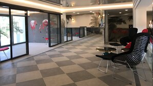 A spacious lobby with a checkered floor, glass walls, and a mural of flamingos. - Park Hotel RAYA Garden (Veliko Tarnovo)