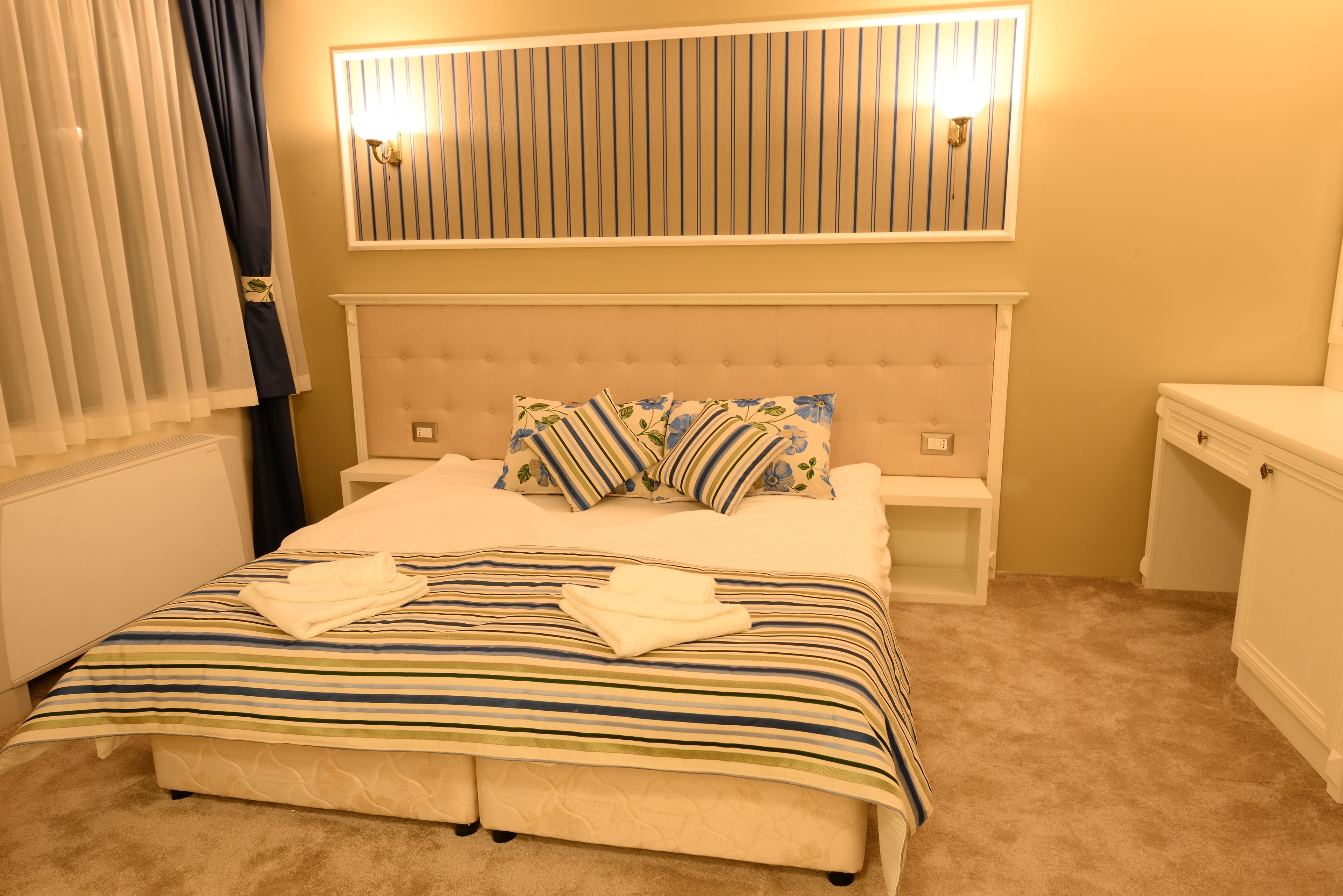 A neatly made bed with striped bedding and pillows, a tufted headboard, bedside tables, and a wall-mounted light fixture.