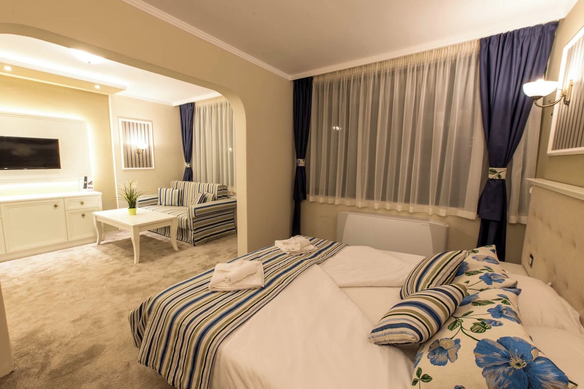 Habitación de hotel con cama, escritorio, silla, televisor y ventana con cortinas.