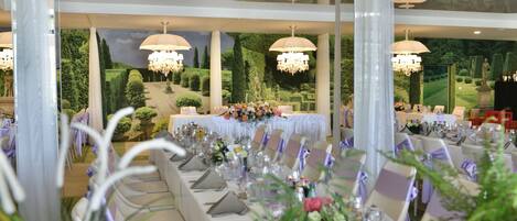 A banquet hall with long tables set for a formal event, adorned with floral centerpieces and elegant table settings.