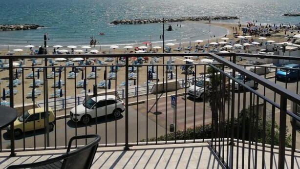 Een balkon met uitzicht op een strand, een pier en verre bergen.