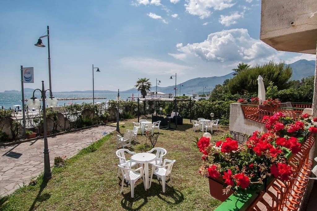 A terrace with outdoor seating, a view of the sea, and a mountainous backdrop.