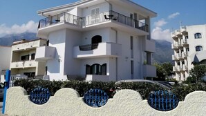 Een modern, tweelaags gebouw met balkons, een verharde oprit en een helderblauwe lucht.