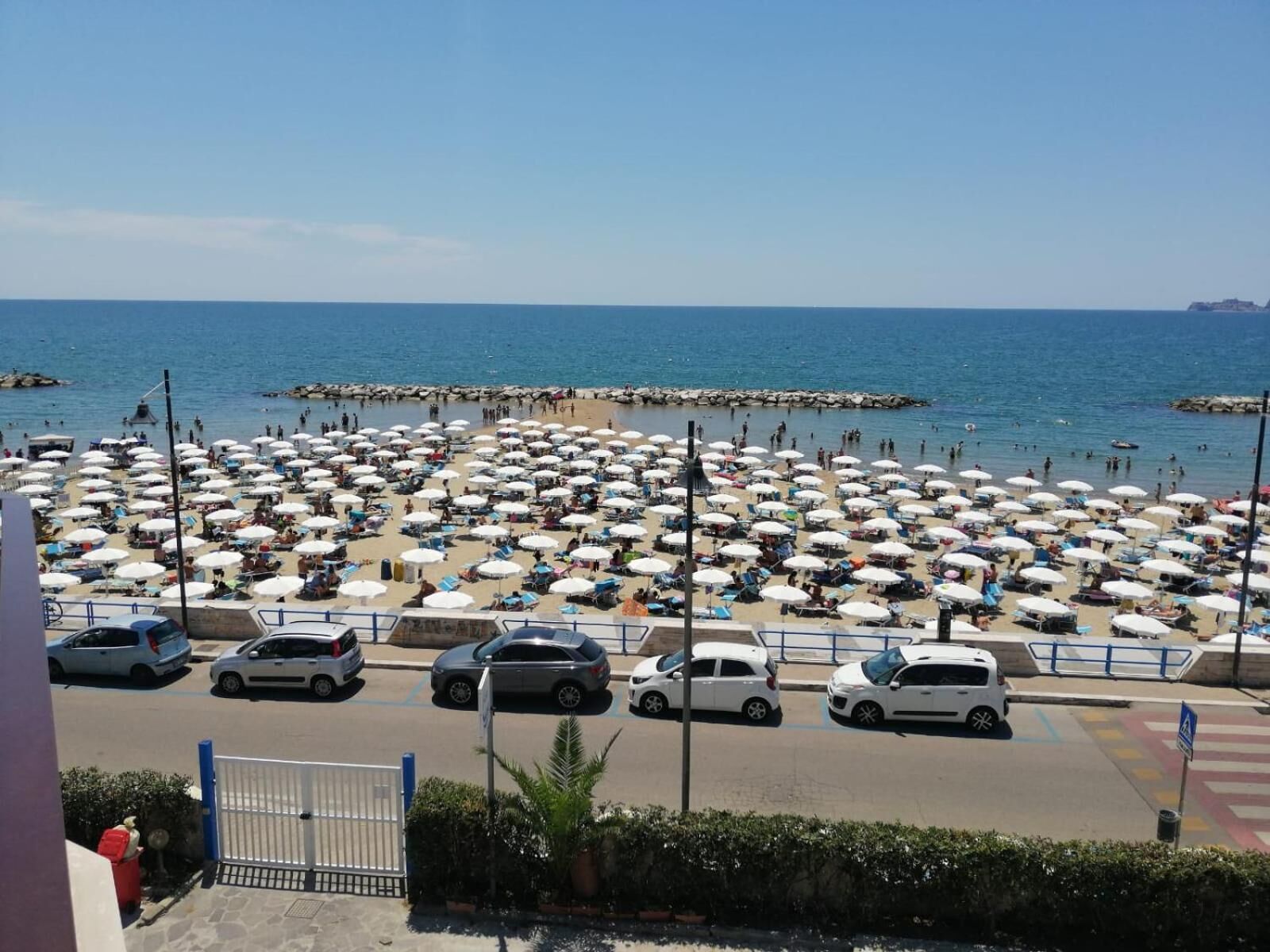 A beach with numerous umbrellas and cars parked along the shore.