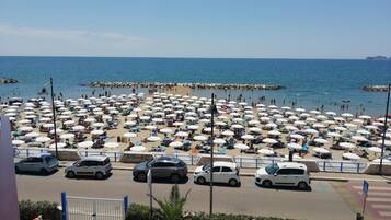 A beach with numerous umbrellas and cars parked along the shore.