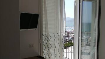 Un balcón con vistas al mar y a las montañas, un televisor en la pared y un escritorio con una silla.