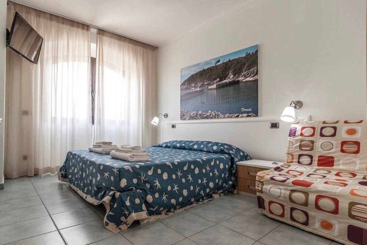 Ein Schlafzimmer mit einem Bett, einem Nachttisch, einer Lampe, einem Gemälde und einem Fenster mit Vorhängen.