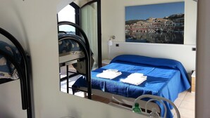 Een slaapkamer met een bed, een raam, een schilderij van een kustplaats en een stoel.