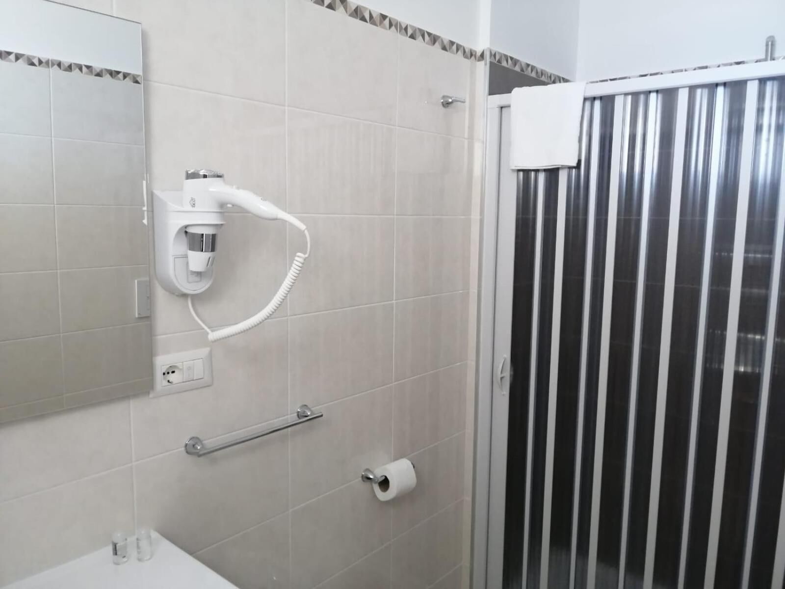 A bathroom with a hairdryer mounted on the wall, a towel rack, a toilet paper holder, and a shower area with a glass door.
