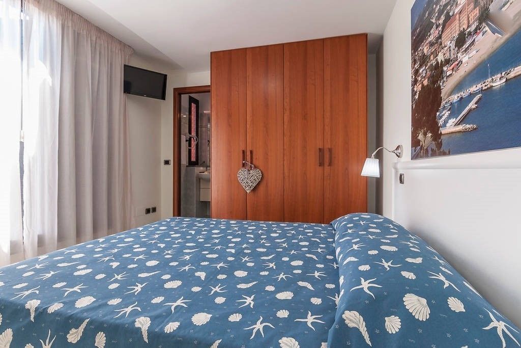 A bedroom with a bed, a wooden wardrobe, a wall-mounted TV, and a poster.