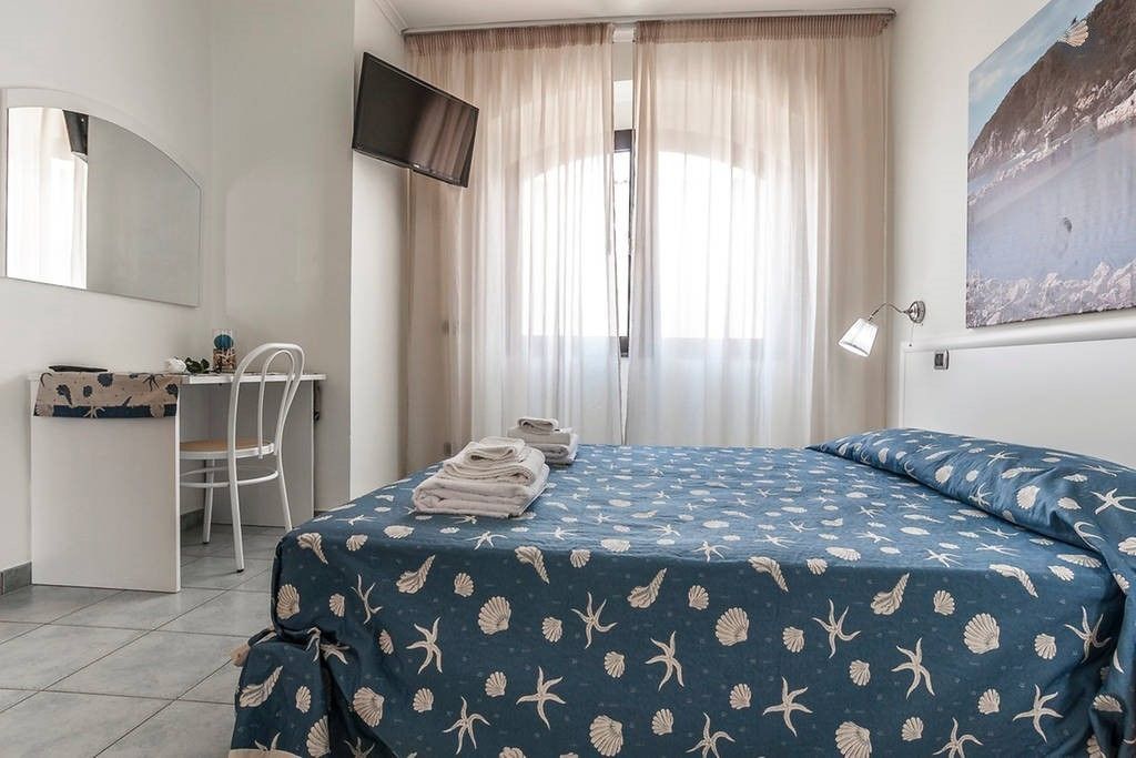 Un dormitorio con cama, escritorio, silla, televisor y ventana con cortinas.