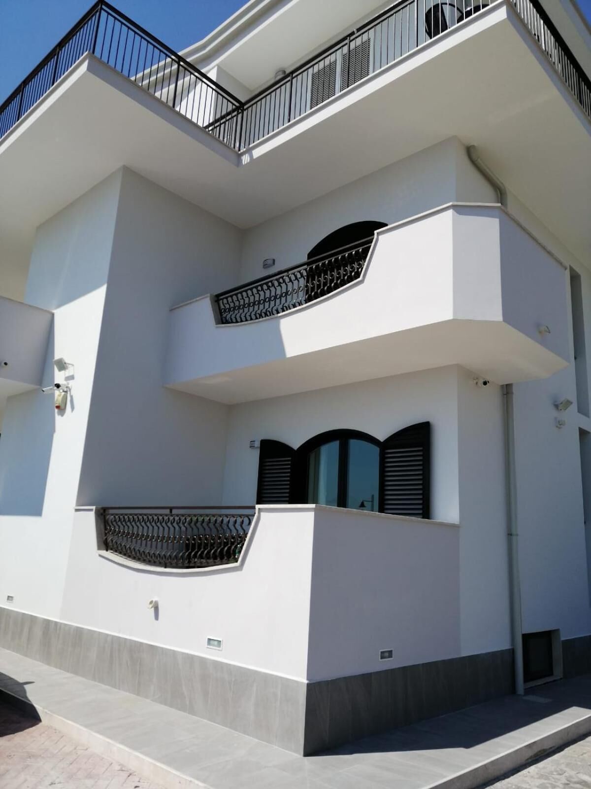 A modern two-story building with a flat roof, white exterior walls, and black metal railings on the balconies.