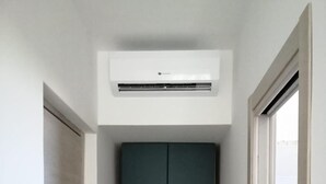 Een smalle gang met een donker kastje, een witte deur aan de rechterkant, en een airconditioningunit erboven.
