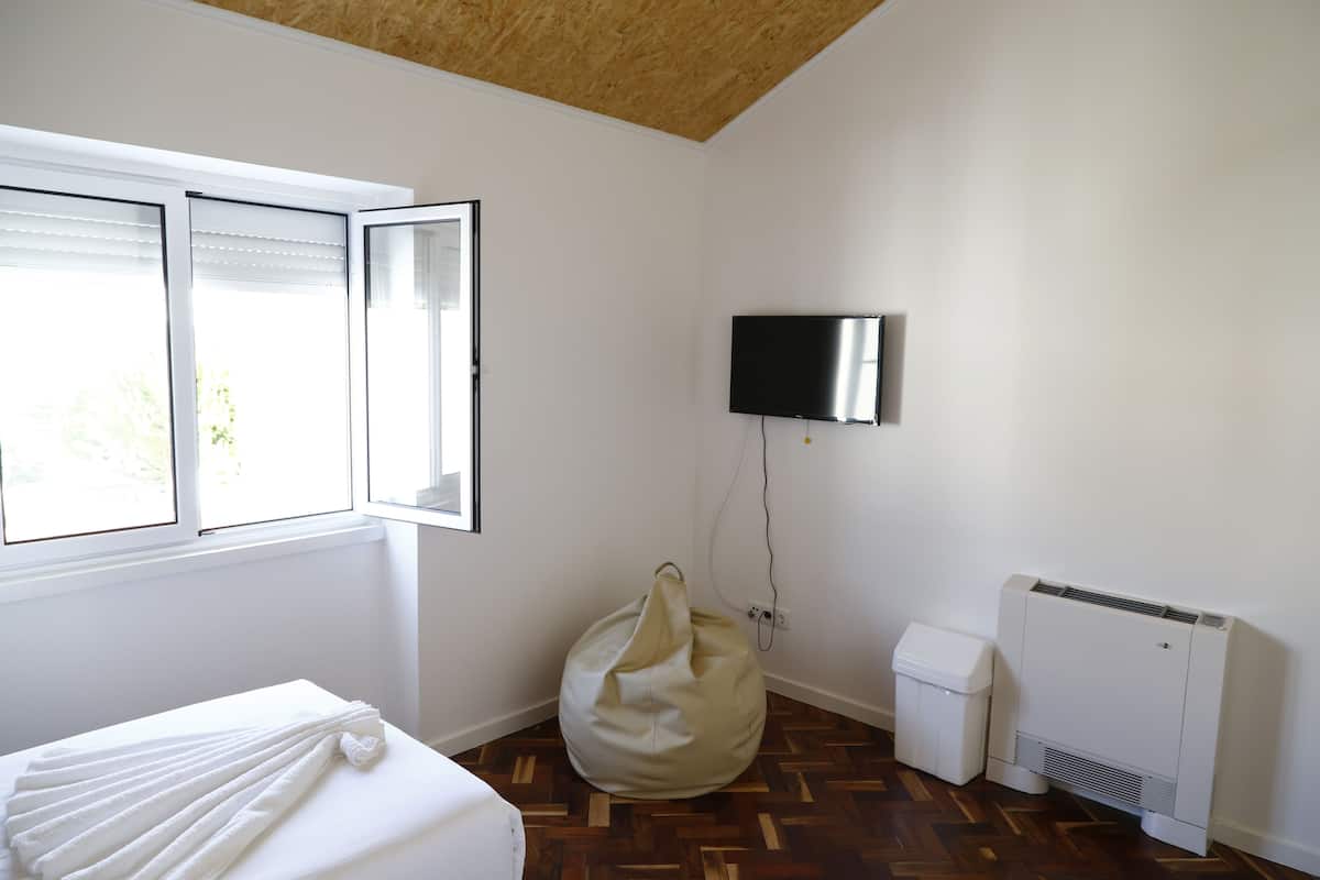 Une chambre avec un lit, un fauteuil poire, une télévision et un radiateur.
