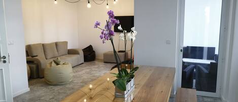 A modern living room with a wooden dining table, a sofa, and a potted plant.