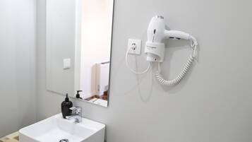Une salle de bain avec un lavabo blanc, un miroir et un sèche-cheveux fixé au mur.
