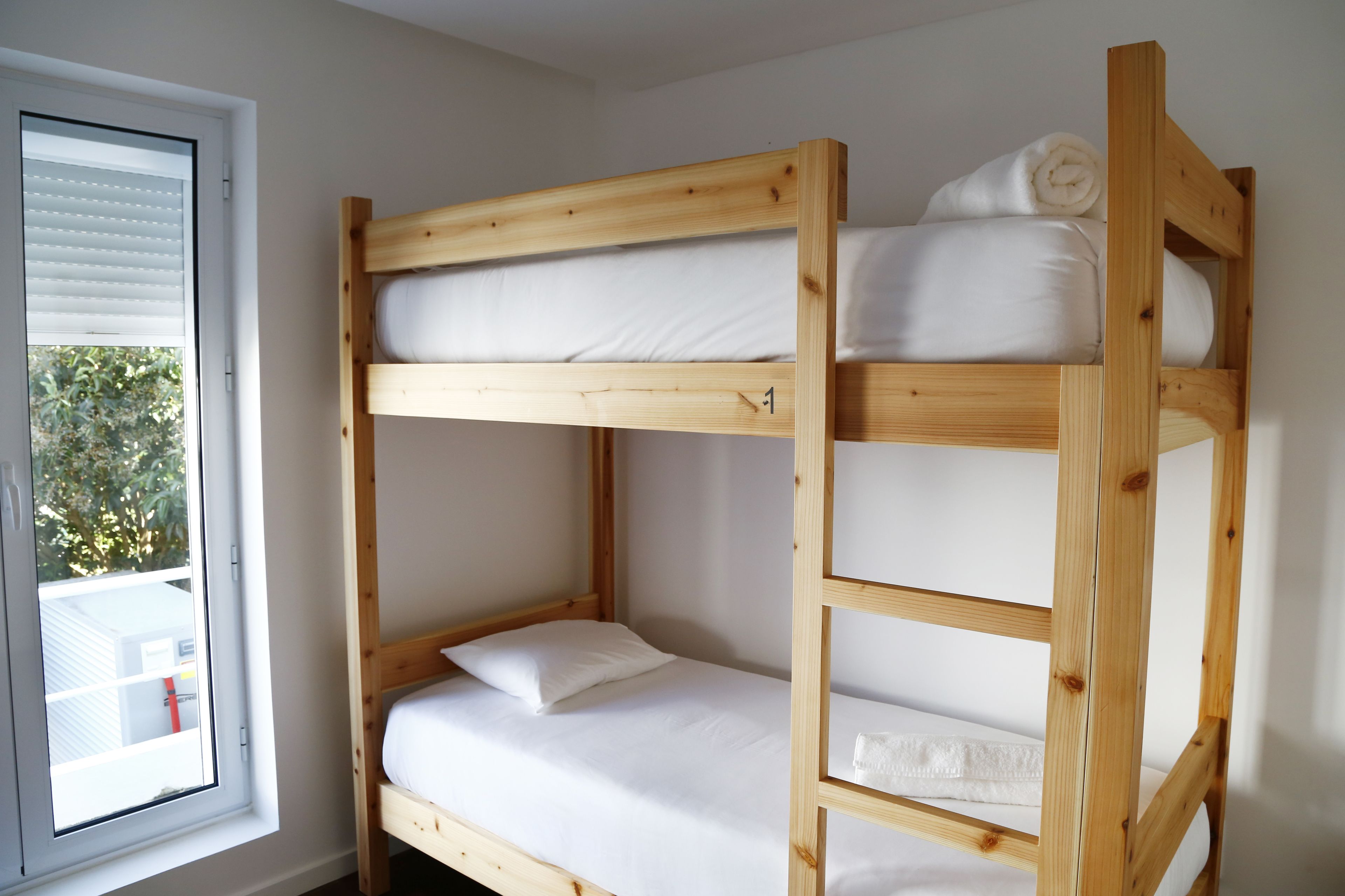 A bunk bed with white bedding and a window with blinds.
