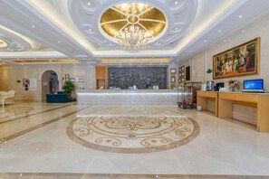 A hotel lobby with a reception desk, a chandelier, and a large painting on the wall.
