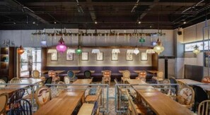 A restaurant interior with wooden tables and chairs, hanging lights, and framed pictures on the wall.