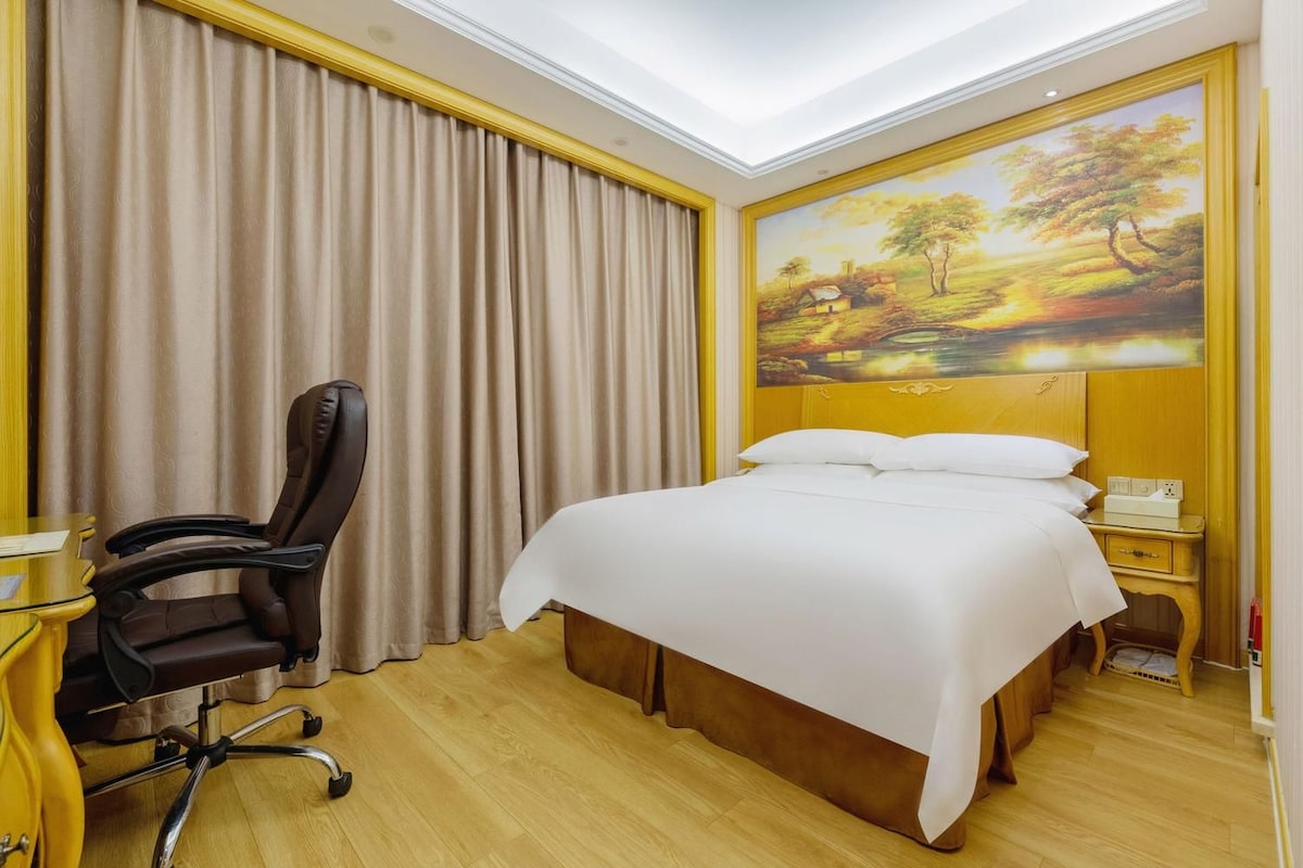 A hotel room with a bed, a desk, a chair, and a painting on the wall.