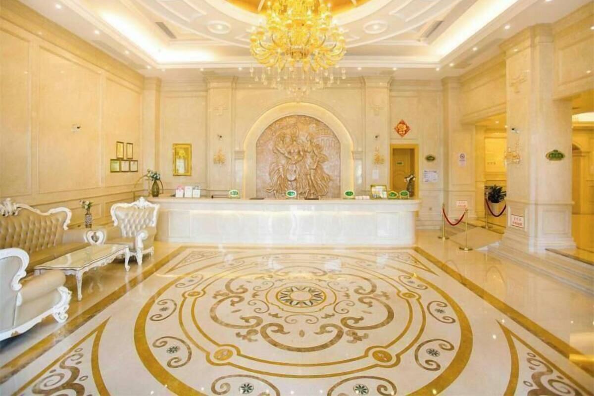 A luxurious lobby with a grand chandelier, a reception desk, and ornate floor design.