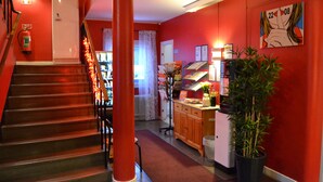 Un vestíbulo de hotel con una escalera, una recepción, un extintor y una planta.